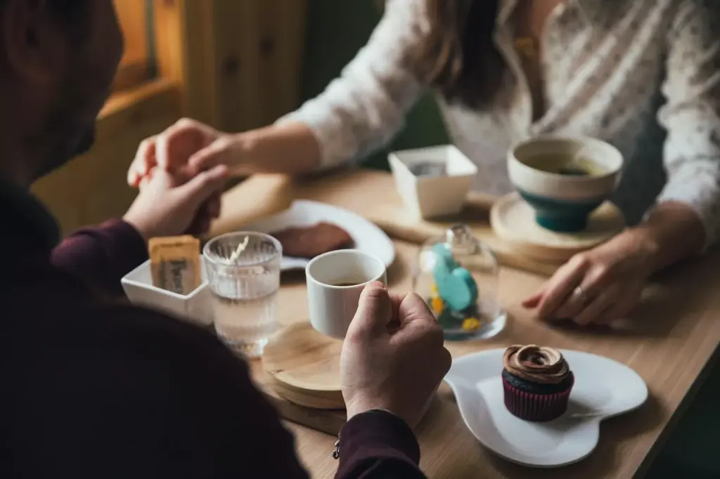 Dos personas tomadas de la mano en la mesa de una cafetería con café y un cupcake