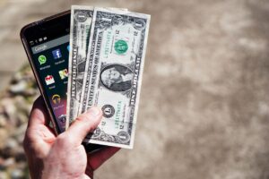 Mano sosteniendo billetes de dólar y un smartphone