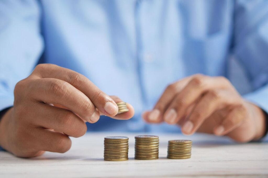 Persona apilando monedas en 3 pilas, cómo ahorrar con salario mínimo por etapas