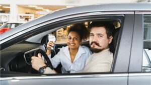 seguro de auto: pareja sonriente dentro de un carro con las llaves en la mano
