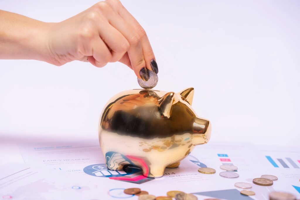 Mano colocando una moneda en una alcancía dorada sobre gráficos de ahorro