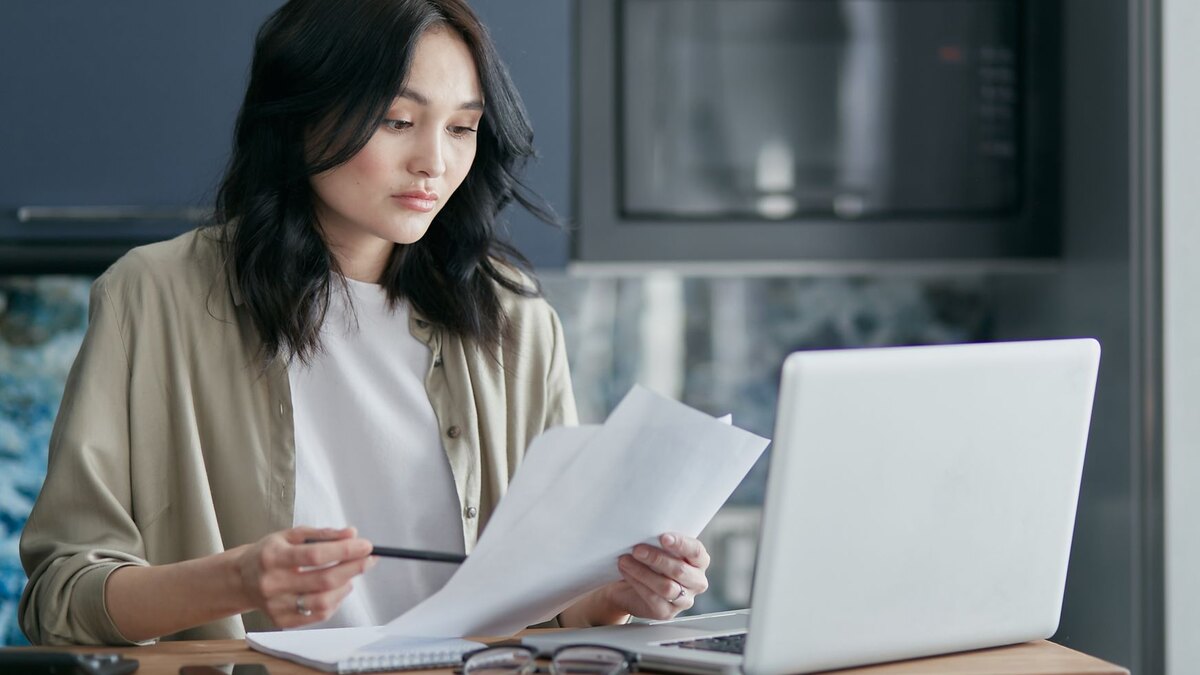 Mujer revisando documentos de impuestos con una computadora en la cocina